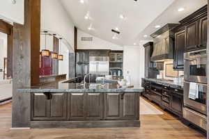 Kitchen featuring a warming drawer, appliances with stainless steel finishes, dark brown cabinets, pendant lighting, and light wood-type flooring