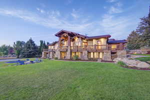 View of front of property featuring a front lawn, stone siding, and a balcony