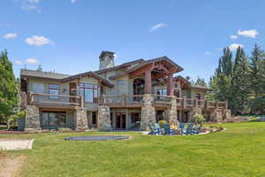 Back of house with a lawn, a chimney, a balcony, and stone siding