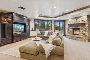 Living area featuring a stone fireplace, light carpet, a raised ceiling, recessed lighting, and ornamental molding