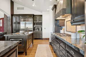 Kitchen featuring glass insert cabinets, custom exhaust hood, light wood-style flooring, vaulted ceiling, and tasteful backsplash