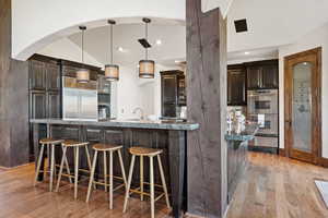 Kitchen featuring a kitchen bar, dark brown cabinets, pendant lighting, light wood-style floors, and appliances with stainless steel finishes