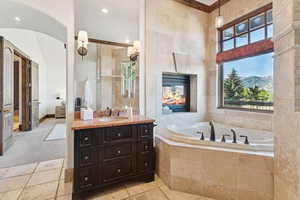 Full bathroom featuring vanity, a garden tub, tile walls, a tiled fireplace, and a mountain view