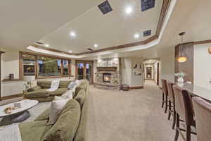 Living room featuring a tray ceiling, light colored carpet, a fireplace, ornamental molding, and recessed lighting