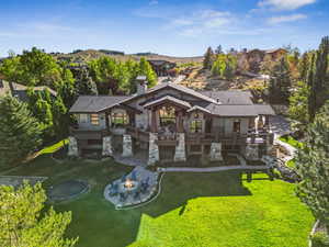 Back of property with a lawn, a fire pit, stone siding, a chimney, and a wooden deck