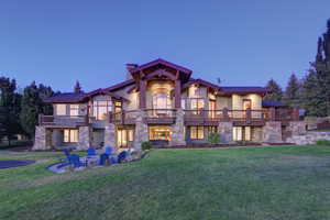 Back of property with a lawn, stone siding, a balcony, and a chimney