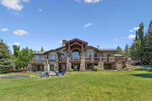 Rear view of property featuring a fire pit, a lawn, a balcony, and a chimney