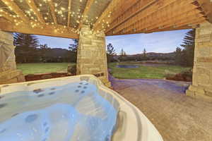 Patio terrace at dusk featuring a lawn, a hot tub, and a patio