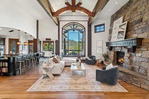 Living room featuring light wood-style flooring, beamed ceiling, a stone fireplace, high vaulted ceiling, and a mountain view