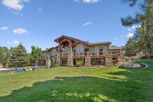 Back of house with a lawn, a balcony, and stone siding