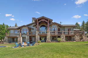 Rear view of house with an outdoor fire pit, a lawn, a balcony, and stone siding