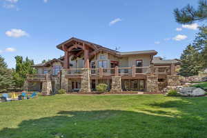 Rear view of house with a yard, a balcony, and stone siding