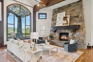 Living area featuring wood finished floors, beamed ceiling, a stone fireplace, and high vaulted ceiling