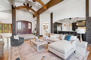 Living room featuring a chandelier, beamed ceiling, a towering ceiling, wood finished floors, and arched walkways