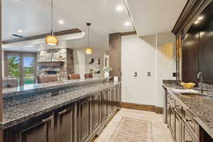 Kitchen featuring decorative light fixtures, dark stone countertops, a tray ceiling, dark brown cabinets, and a stone fireplace