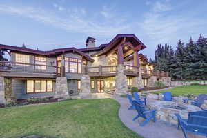 Back of property at dusk featuring a yard, a fire pit, a chimney, a patio, and stone siding