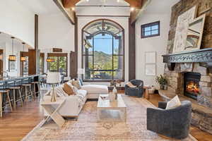 Living room featuring light wood finished floors, high vaulted ceiling, beamed ceiling, a mountain view, and a stone fireplace
