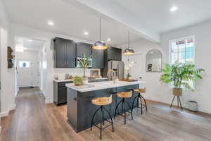 Kitchen featuring healthy amount of natural light, hanging light fixtures, a breakfast bar area, light wood-style floors, and recessed lighting
