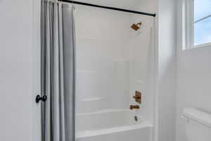 Full bathroom featuring shower / bath combination with curtain and toilet