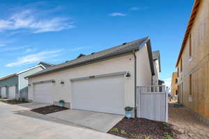 View of side of home featuring stucco siding, a shingled roof, driveway, and a garage
