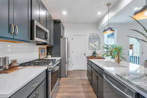 Kitchen with appliances with stainless steel finishes, light stone counters, light wood-type flooring, pendant lighting, and recessed lighting