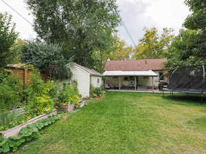 View of green lawn featuring a trampoline, a garden, and a patio area