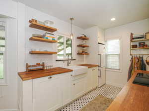 Kitchen featuring butcher block countertops, open shelves, backsplash, pendant lighting, and healthy amount of natural light