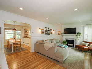 Living area featuring arched walkways, light wood finished floors, recessed lighting, a tiled fireplace, and ornamental molding