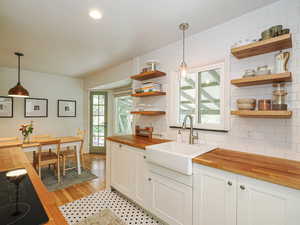 Kitchen featuring butcher block countertops, decorative light fixtures, backsplash, open shelves, and black electric cooktop