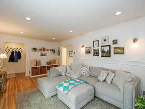 Living area featuring arched walkways, wood finished floors, recessed lighting, crown molding, and a wainscoted wall