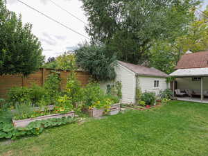 View of yard featuring a vegetable garden, a patio area, and an outbuilding