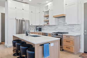 Kitchen featuring appliances with stainless steel finishes, decorative backsplash, a breakfast bar area, open shelves, and white cabinets