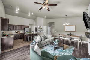 Living room featuring arched walkways, a ceiling fan, a chandelier, light wood-style floors, and vaulted ceiling