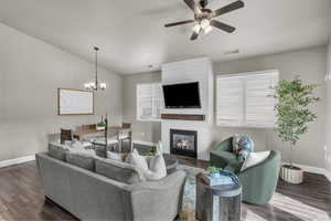 Living room featuring healthy amount of natural light, a large fireplace, dark wood-style flooring, and a chandelier