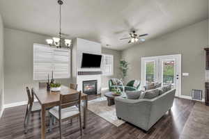 Living room with a fireplace, lofted ceiling, dark wood-type flooring, a ceiling fan, and a chandelier