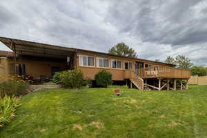 Back of property featuring a lawn, brick siding, a wooden deck, and stairs