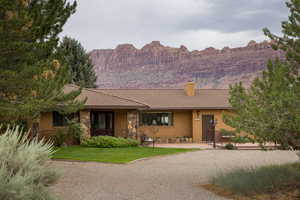 Ranch-style house featuring a chimney, brick siding, a front lawn, a mountain view, and stone siding