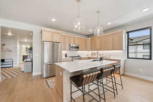 Kitchen with light brown cabinets, appliances with stainless steel finishes, light wood-style floors, and recessed lighting