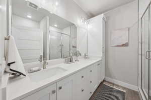Full bath with double vanity, a marble finish shower, and dark wood-type flooring