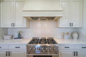 Kitchen with custom exhaust hood, high end stainless steel range oven, white cabinets, and backsplash
