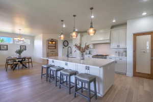 Kitchen featuring a breakfast bar area, an island with sink, decorative light fixtures, white cabinets, and recessed lighting