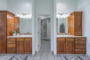 Bathroom with light tile patterned flooring, two vanities, and a walk in closet