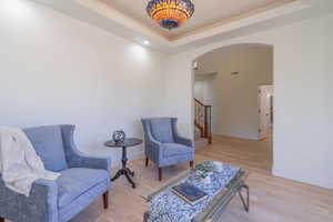 Sitting room with arched walkways, light wood-style flooring, a tray ceiling, and stairs
