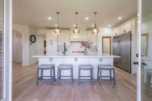Kitchen with a large island with sink, light wood-style flooring, decorative backsplash, a breakfast bar, and recessed lighting
