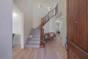 Foyer featuring arched walkways, light wood-style floors, a towering ceiling, and stairs