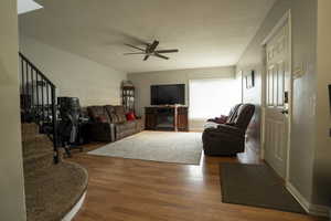 Living area featuring stairs, a glass covered fireplace, wood finished floors, and ceiling fan