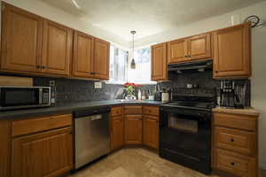 Kitchen with appliances with stainless steel finishes, brown cabinets, backsplash, and a textured ceiling