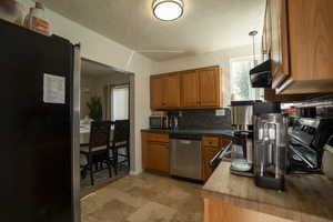 Kitchen featuring stainless steel appliances, backsplash, brown cabinetry, a textured ceiling, and extractor fan