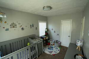 Bedroom with dark carpet, a nursery area, and a textured ceiling
