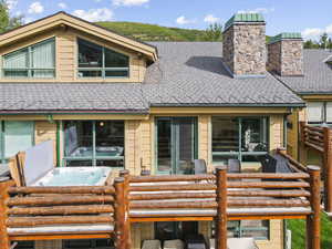 Back of house with a chimney, a hot tub, and a shingled roof